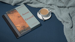Book titled "Aces Across Ground" with coffee cup on blue surface beside gray textile.