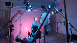 Studio portrait lit with multiple professional lights creating a pink and blue color cast on the subject.