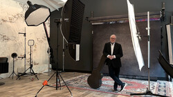 Man in business attire standing in a professional photography studio with softbox lighting and reflector equipment.