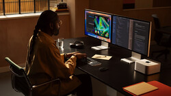 Creative professional working at a dual-monitor setup with colorful data visualization displayed on screen.