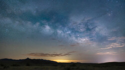Milky Way galaxy stretches across a starry night sky above a desert landscape at twilight.