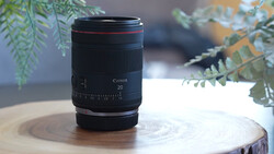 Canon RF 20mm lens displayed on a wooden surface with green foliage in the background.