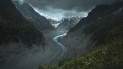 Winding river cuts through a dramatic mountain valley beneath storm clouds.