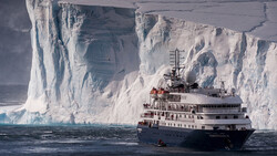 Expedition ship navigating alongside towering white ice cliffs in polar waters.