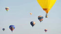 Multiple hot air balloons in flight against a clear blue sky at various altitudes and distances.