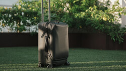 Black hardside rolling suitcase with extended handle standing on grass outdoors.