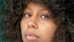 Portrait of a woman with curly dark hair looking upward with a contemplative expression.