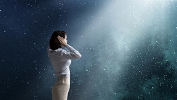 Woman in white shirt gazing upward amid falling particles and ethereal light rays.