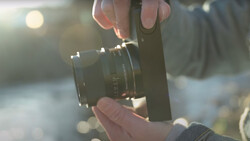 Photographer's hands holding a vintage manual focus lens against a blurred outdoor background in golden sunlight.