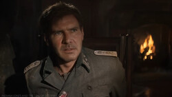 Man in military uniform seated before a fireplace with warm amber lighting.