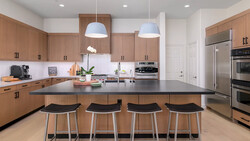 Modern kitchen with wood cabinetry, black island countertop, and four black bar stools under pendant lighting.