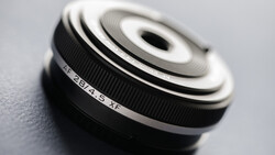 Compact prime lens with fixed focal length mounted on neutral surface, showing ribbed focus ring and depth-of-field markings.