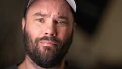Bearded man wearing a light gray cap, looking directly at camera with a serious expression.