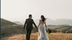 Bride and groom walking hand-in-hand through a golden harvest field at dusk.