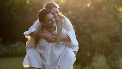 Man in white shirt giving piggyback ride to woman in golden-hour sunlight.