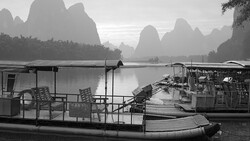 Moored boats on still water with dramatic limestone peaks shrouded in mist in the background.