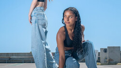 Two women posing on a rooftop against a clear blue sky, wearing distressed denim jeans and crop tops.