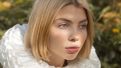 Young woman with shoulder-length blonde hair wearing a white textured garment, photographed outdoors with soft natural lighting.