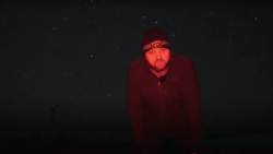 Person wearing deep red jacket and beanie with headlamp in dark night setting with stars.