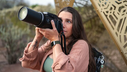 Woman holding vintage film camera up to her face, looking through viewfinder outdoors.