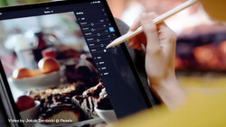 Photographer using stylus on tablet displaying food photography with adjustment panel open.
