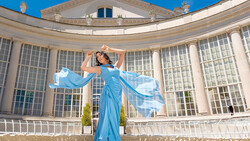Woman in flowing blue gown with fabric in motion against classical columned building facade.