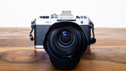 OM System OM-3 rangefinder camera with attached zoom lens on wooden surface.