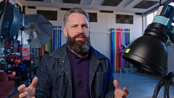 Bearded man speaking in a professional studio with professional lighting equipment visible.