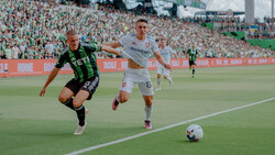 Two soccer players competing for the ball during a match in a crowded stadium.