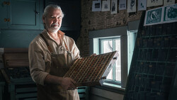 Craftsman holding a wooden sample board with diagonal wood grain pattern in his workshop.