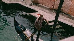 Gondolier in striped shirt standing in gondola at dock, preparing boat or waiting for passengers.