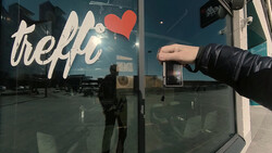 Hand reaching toward a glass storefront door with "hello" text and red heart decal.