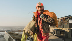 Commercial fisherman holding large caught fish at a harbor dock at sunrise.