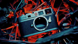 Leica M9 rangefinder camera body positioned on vibrant red and blue neon-lit cables and wires.