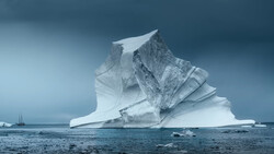 Massive iceberg with dramatic angular formations floating in dark blue ocean water.