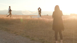 Four people standing in a dry, golden field at golden hour with backlighting creating silhouettes.