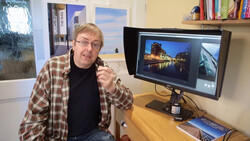 Photographer in plaid shirt at desk reviewing architectural images on dual monitors.
