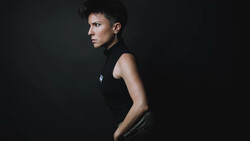 Person in black sleeveless top photographed in profile against dark background.