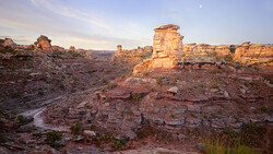 Golden-hour sunlight illuminates layered sandstone formations and rock outcroppings in an arid canyon landscape.