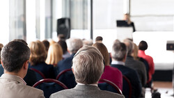 Rear view of audience members seated in rows during an indoor presentation or conference event.