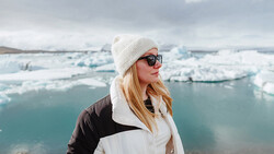 Woman in winter clothing overlooking a glacial lake filled with icebergs.