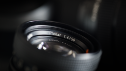 Close-up of a Planar 1.4/50mm lens with shallow depth of field and dramatic lighting against a dark background.
