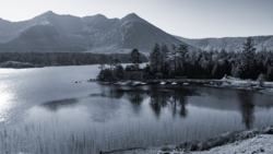 Snow-covered mountains and coniferous forest reflected in a partially frozen alpine lake.