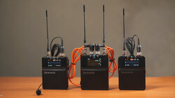 Three Saramonic wireless microphone transmitter units arranged on a wooden surface with cables and antennas.