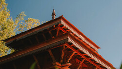 Red-orange tiered pagoda roof with ornate wooden beams against blue sky and golden foliage.