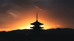 Silhouetted Asian pagoda backlit by a golden sunset sky with dramatic clouds.