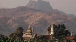 Buddhist temple complex with golden spires nestled in a valley beneath misty mountains.