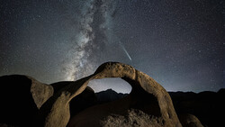Milky Way galaxy stretching above a natural rock arch formation under a starry night sky.