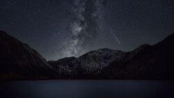 Milky Way galaxy arches over a dark mountain landscape reflected in still water below.