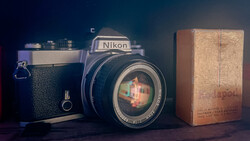 Vintage Nikon film camera with leather case and wooden film box arranged on dark surface.